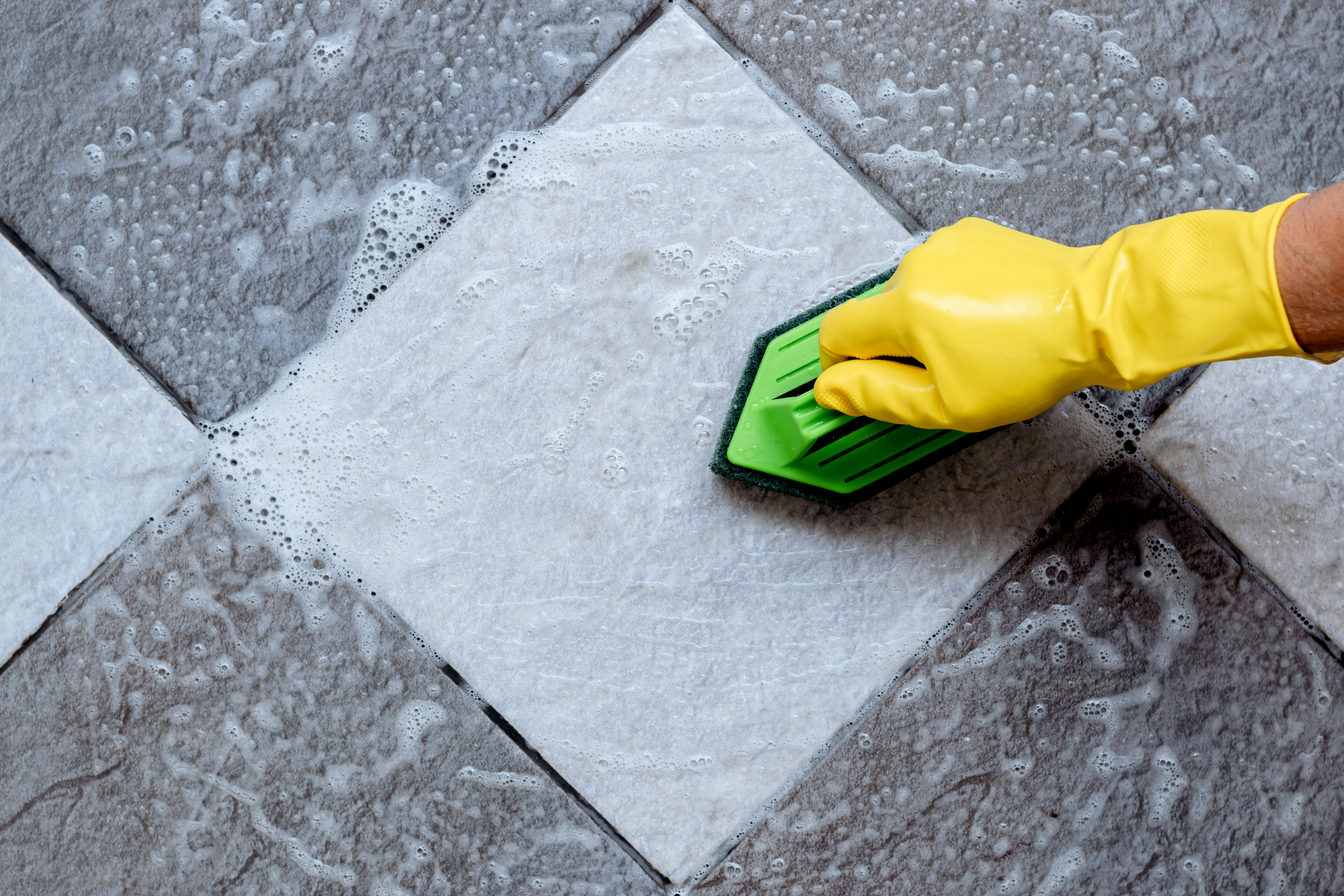 cleaning the tiled floor with a green color plastic floor scrubber.